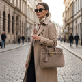 Woman carrying the textured taupe handbag with gold padlock closure on a city street